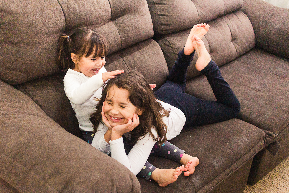 Foto de irmãs brincando no sofá de casa no ensaio lifestyle infantil na cidade de Franco da Rocha em São Paulo