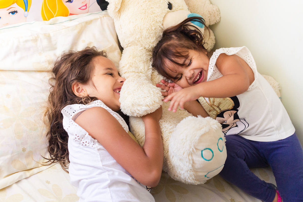 Foto de irmãs se abraçando na cama do quarto no ensaio infantil em casa na cidade de Franco da Rocha- São Paulo