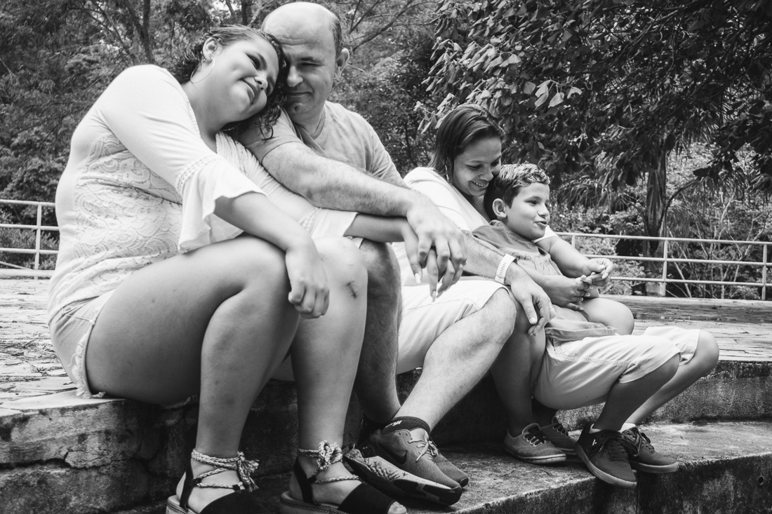 Foto de pais e filhos juntos sentados se abraçando no ensaio externo lifestyle no parque do Carmo em São Paulo