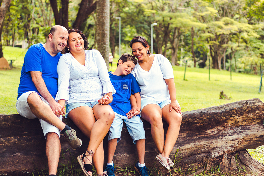 Foto de pais e filhos juntos sentados no tronco da árvore se abraçando no ensaio externo lifestyle no parque do Carmo em São Paulo