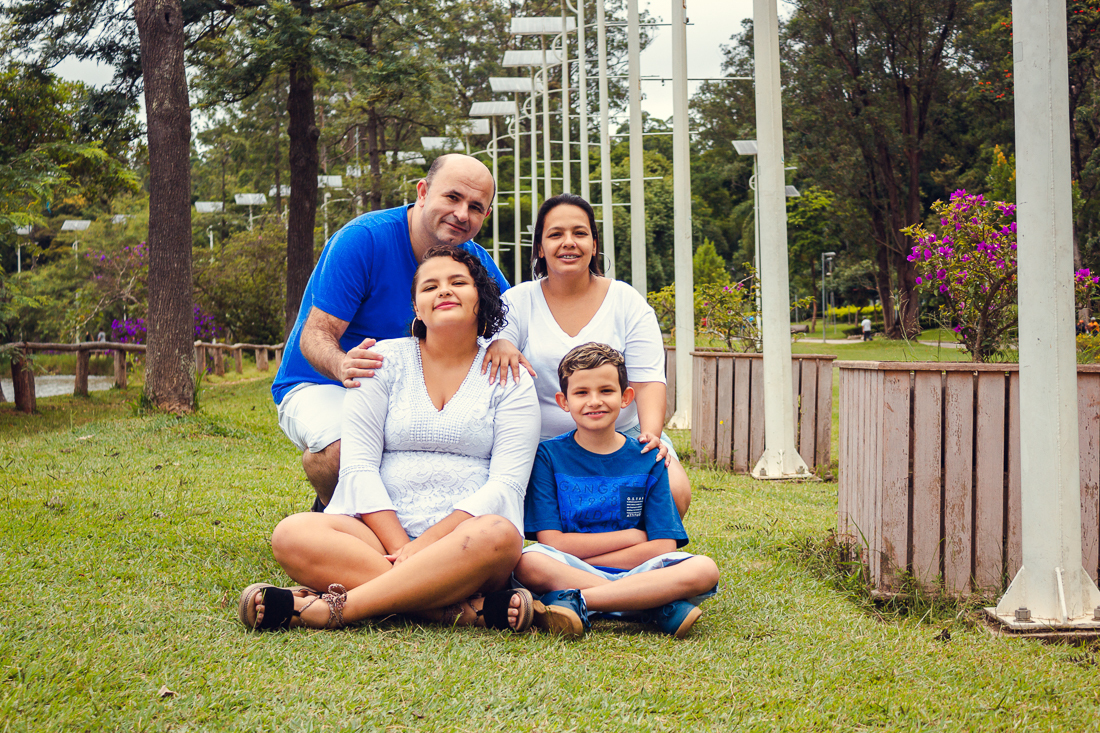 Foto de pais e filhos juntos sentados na grama no ensaio externo lifestyle no parque do Carmo em São Paulo