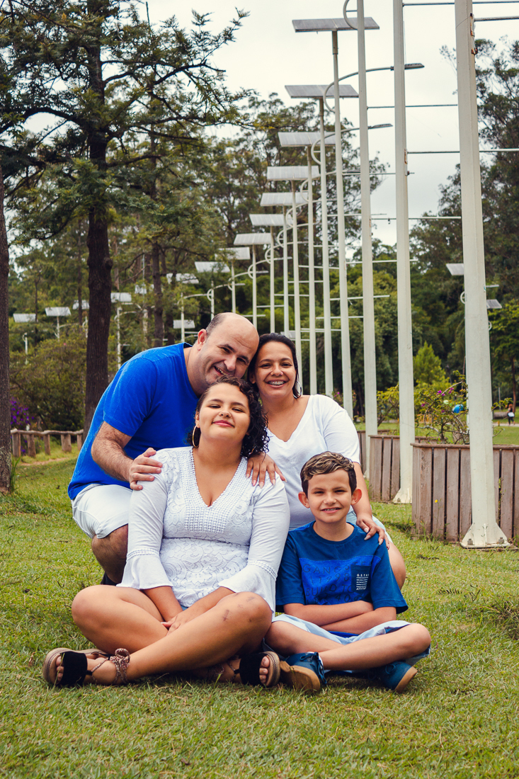 Foto de pais e filhos juntos sentados na grama se abraçando no ensaio externo lifestyle no parque do Carmo em São Paulo