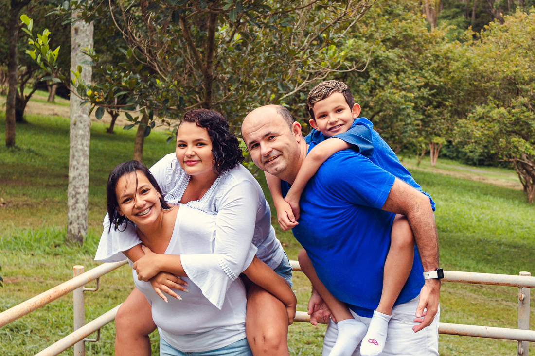 Foto de pais e filhos brincando de cavalinho no colo no ensaio externo lifestyle no parque do Carmo em São Paulo