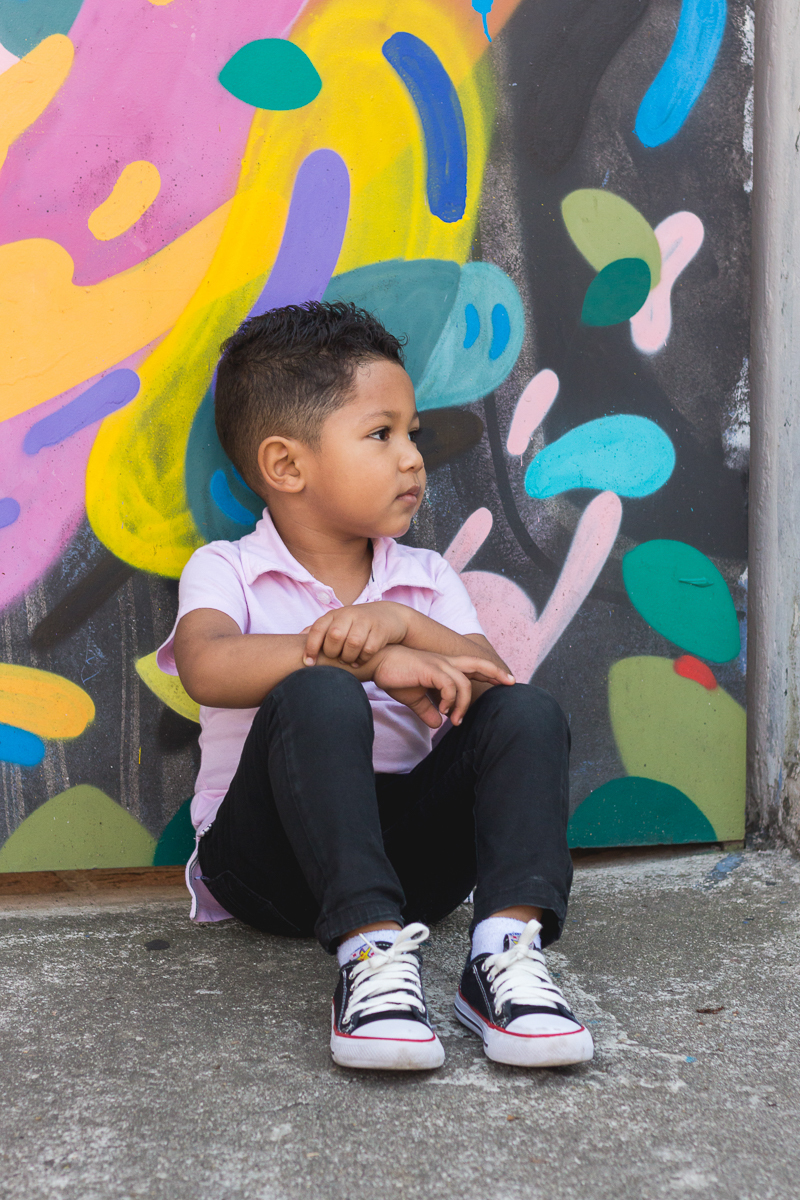 foto de menino fazendo pose sentado no chão no ensaio infantil realizado Beco do Batman na cidade de São Paulo