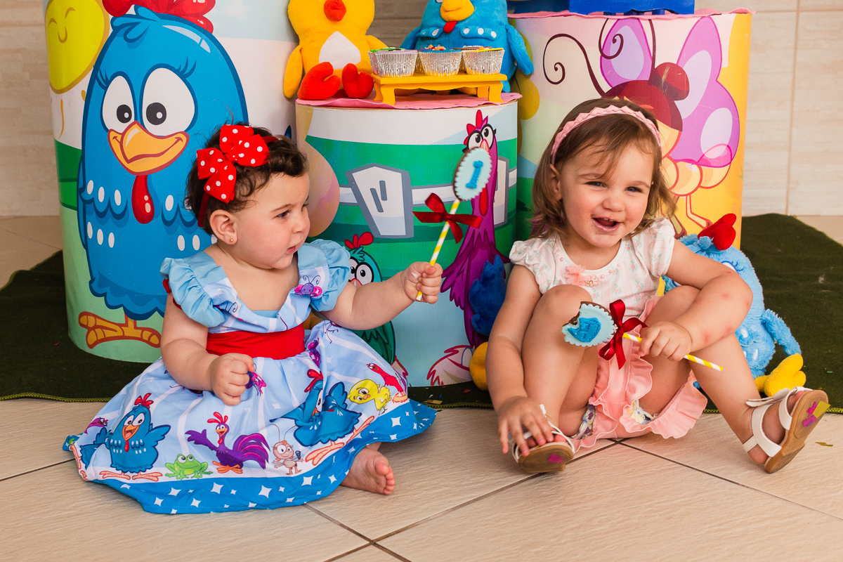 foto de irmãs sentadas no chão em frente a mesa da decoração no aniversario infantil na cidade de São Paulo