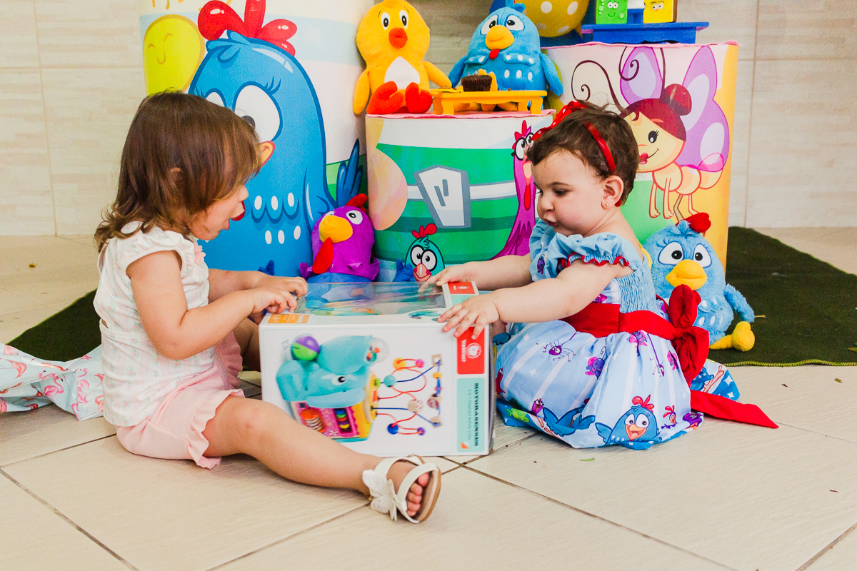 foto de irmãs sentadas no chão abrindo os presentes em frente a mesa da decoração no aniversario infantil na cidade de São Paulo