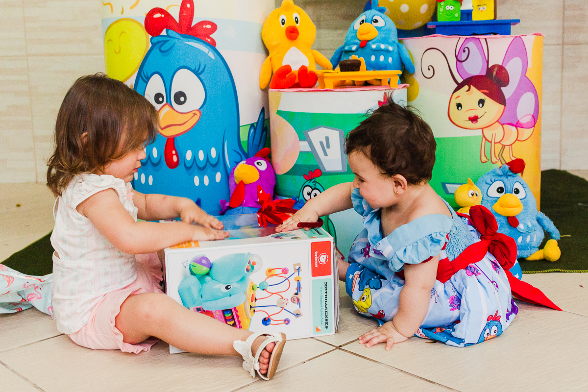 foto de irmãs sentadas no chão abrindo os presentes em frente a mesa da decoração no aniversario infantil na cidade de São Paulo