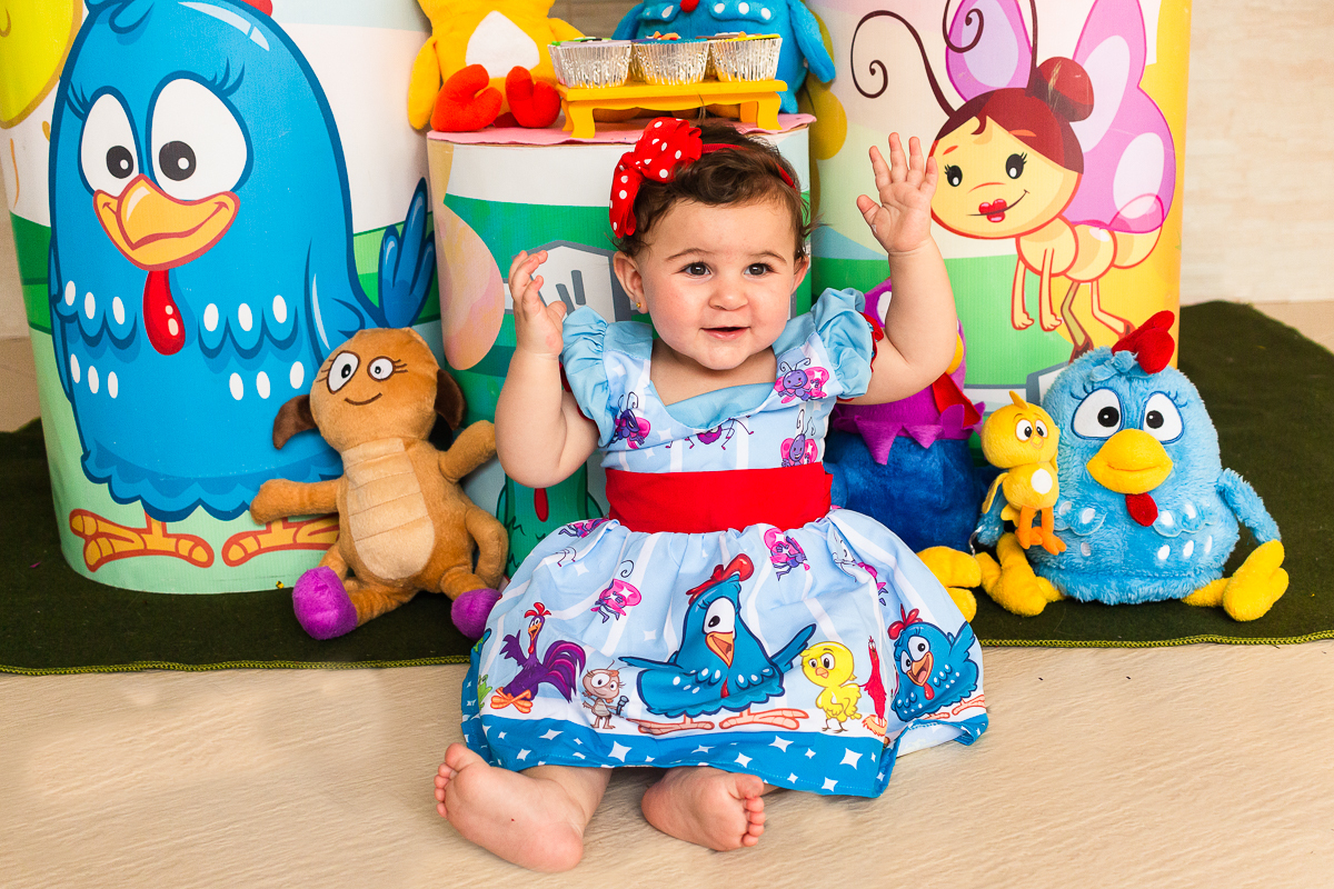 foto da aniversariante com vestido da galinha pintadinha  sentada no chão em frente a mesa da decoração