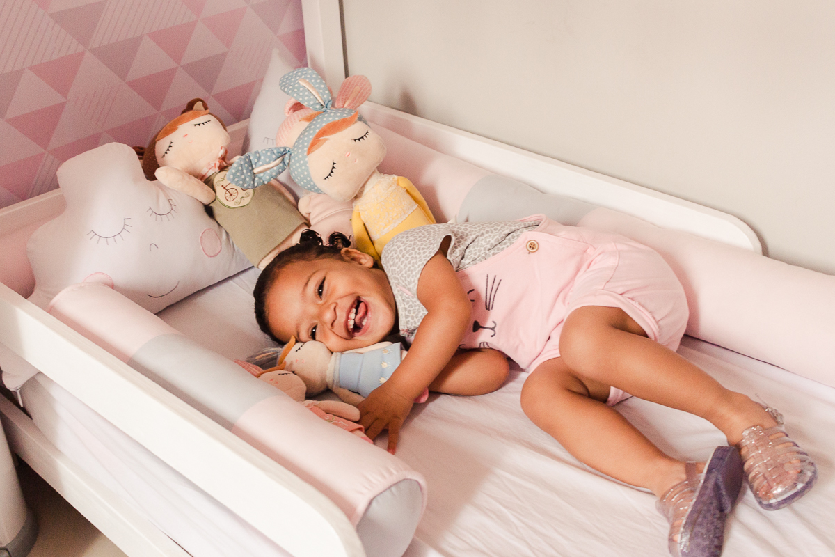 foto infantil de criança deitada dentro do berço com boneca metoo no ensaio de família em casa na zona sul da cidade de Sp