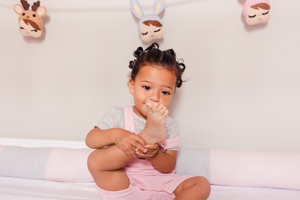 foto de menina dentro do berço olhando para o pé descalço, no ensaio de família em casa na zona sul da cidade de Sp