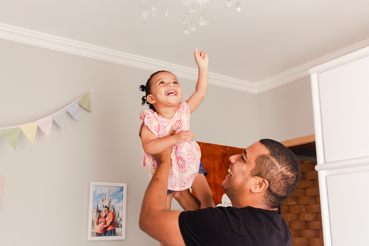foto de menina sorrindo segurada pelo pai dentro do quarto 