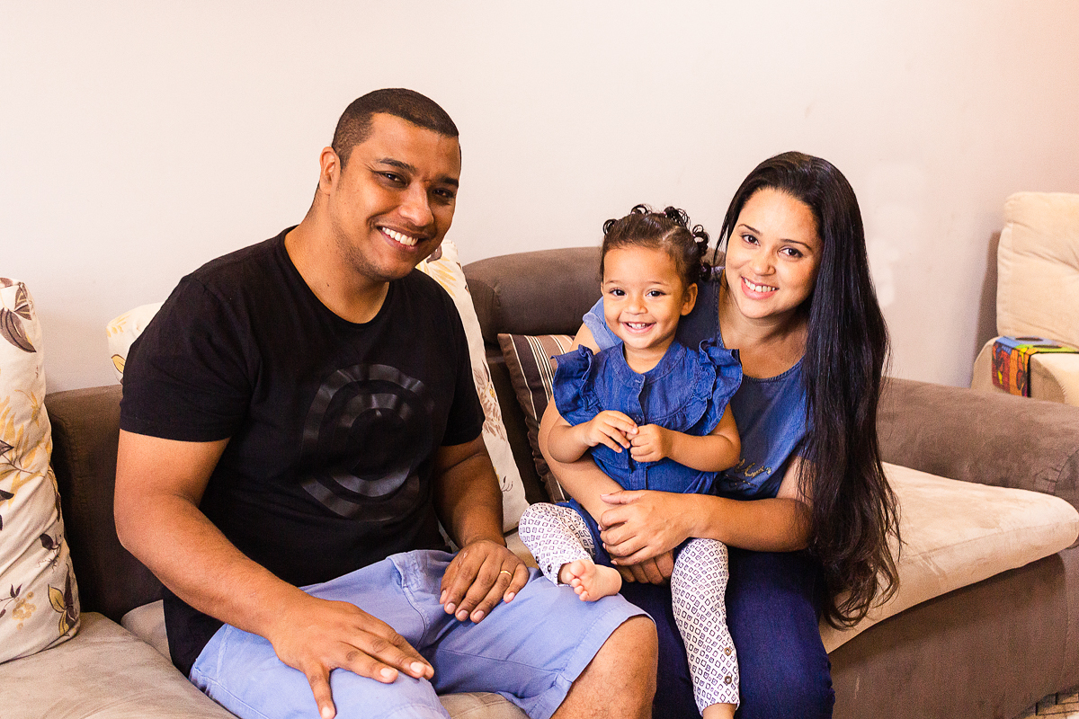 foto de família sorrindo sentados no sofá da sala no ensaio lifestyle em casa na cidade de SP