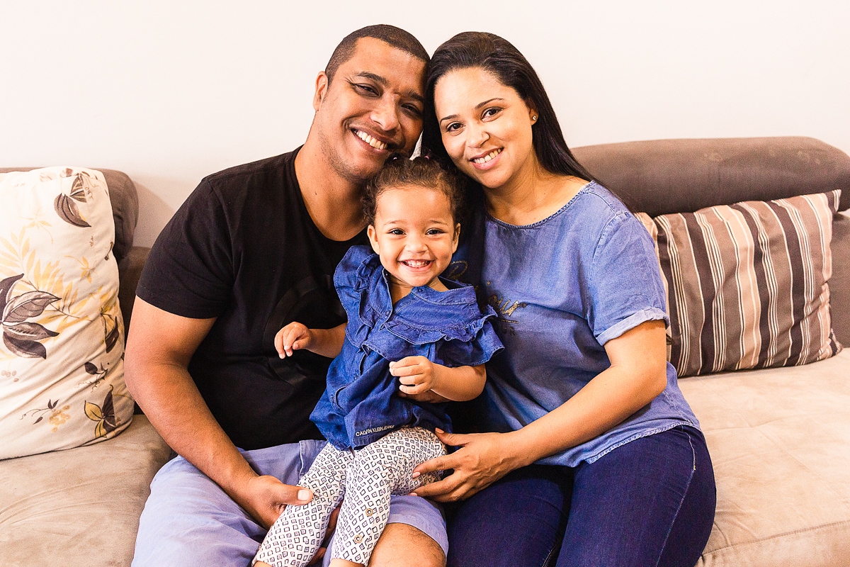 foto de família sorrindo sentados no sofá da sala no ensaio lifestyle em casa na cidade de SP