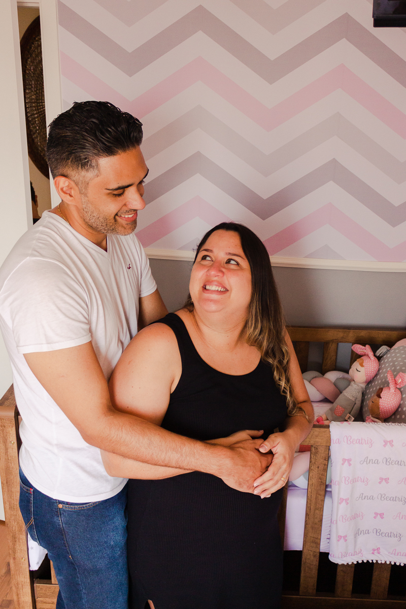 Foto do casal mãe e pai a espera da bebe menina se olhando no quarto no ensaio de família na cidade de Sp