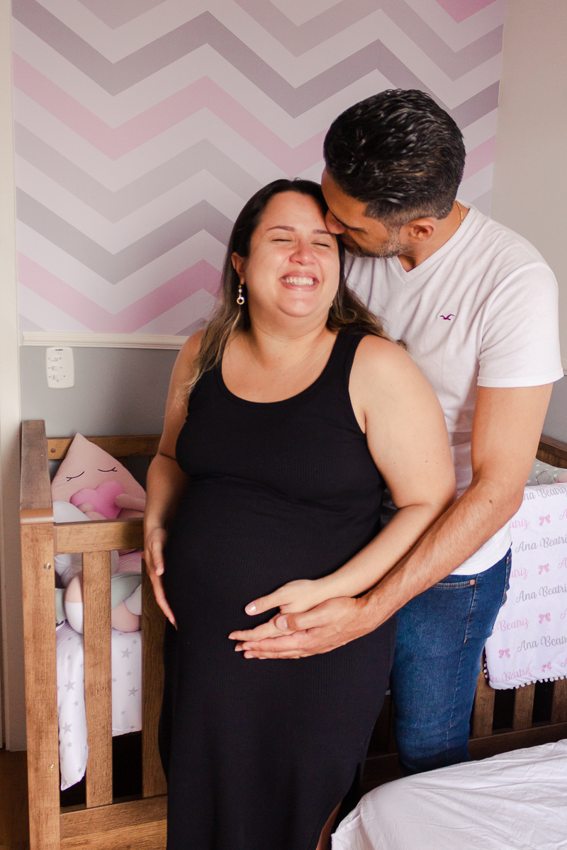 Foto do casal mãe e pai a espera da bebe menina com a mão na barriga no quarto no ensaio de gestante na cidade de Sp