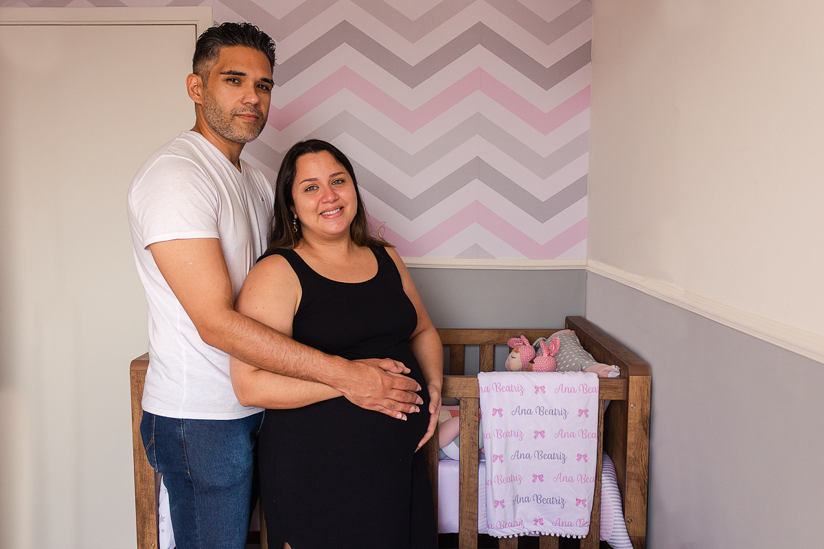 Foto do casal mãe e pai a espera da bebe menina com a mão na barriga no quarto no ensaio de gestante na cidade de Sp