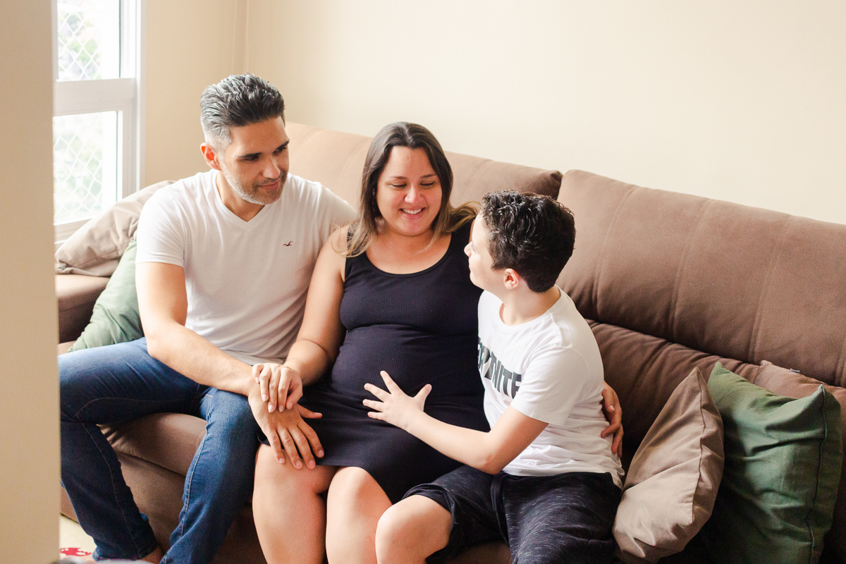 foto de mãe filho e marido sentados no sofá da sala no ensaio de gestante na cidade de Sp