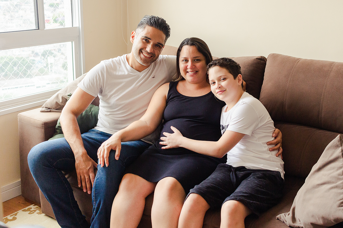 foto de mãe filho e marido sentados no sofá da sala no ensaio de gestante na cidade de Sp