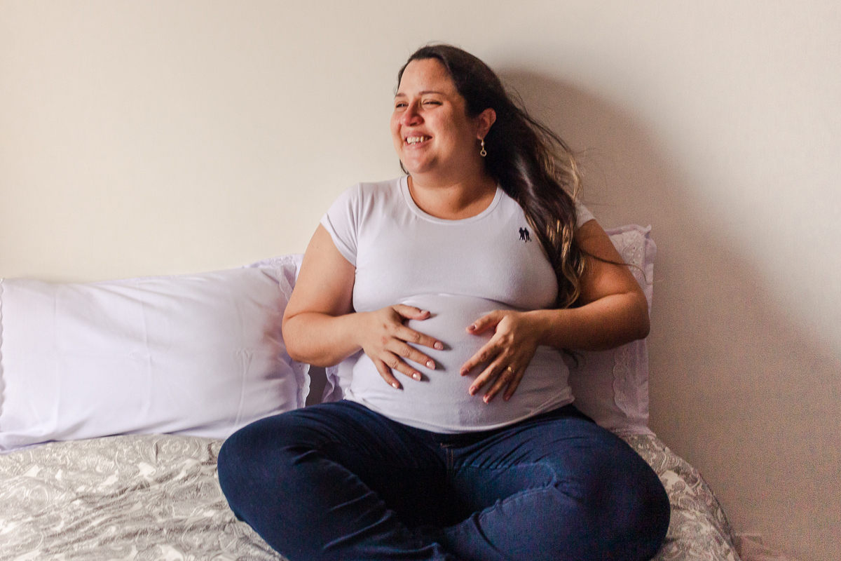 foto de mamãe na cama do quarto sorrindo com a mão na barriga no ensaio lifestyle de gestante na cidade de Sp 