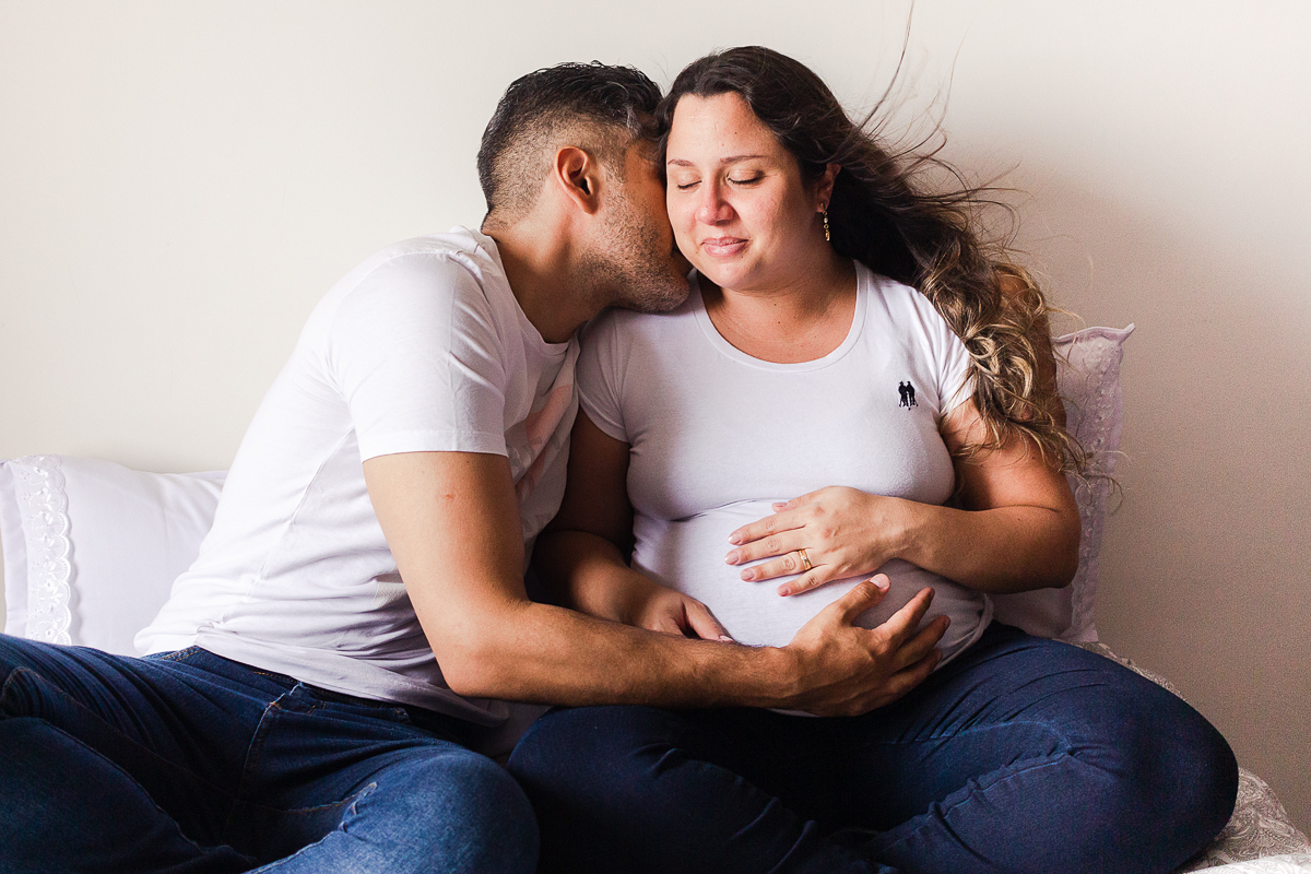 foto de casal abraçados na cama com a mão na barriga de gravida no ensaio de gestante em Sp