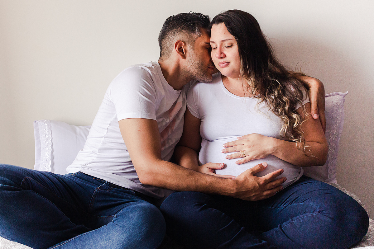 foto de casal abraçados na cama com a mão na barriga de gravida no ensaio de gestante em Sp