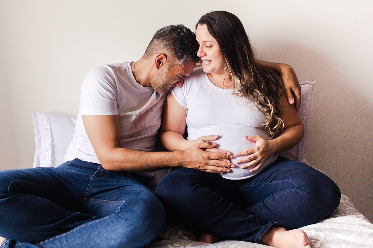 foto de casal abraçados na cama com a mão na barriga de gravida no ensaio de gestante em Sp