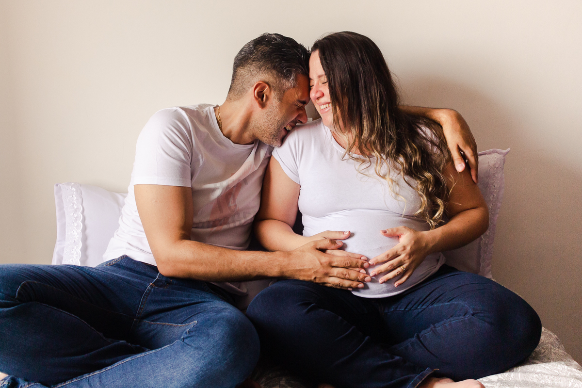 foto de casal abraçados sorrindo com a mão na barriga de gravida no ensaio de gestante em Sp