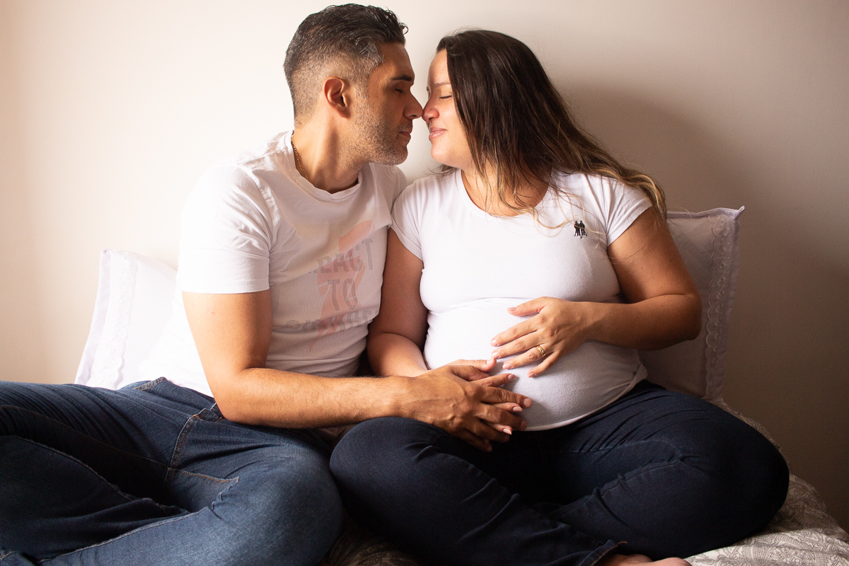 foto de casal abraçados na cama com a mão na barriga de gravida no ensaio de gestante em Sp
