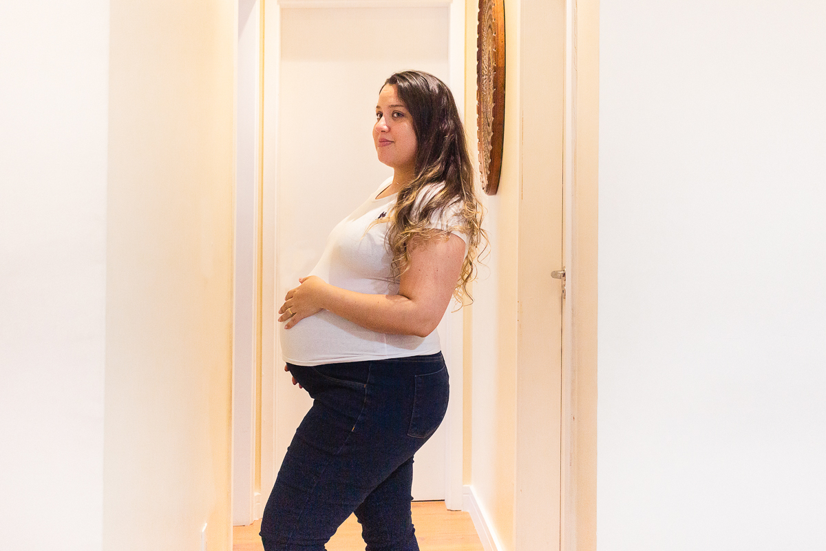 foto de mamãe gravida com a mão na barriga com pose no corredor do apartamento no ensaio de gestante na cidade de Sp