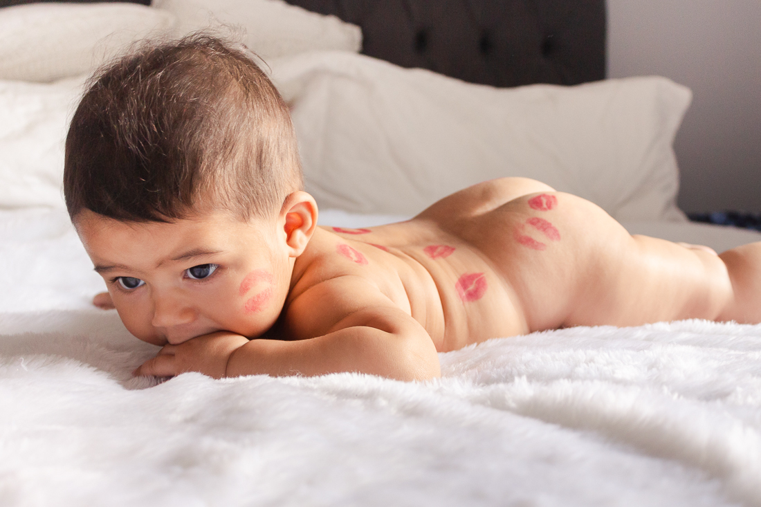 foto infantil de bebe deitado na cama do quarto dos pais pelado com beijo de batom no ensaio de família na cidade de Sp