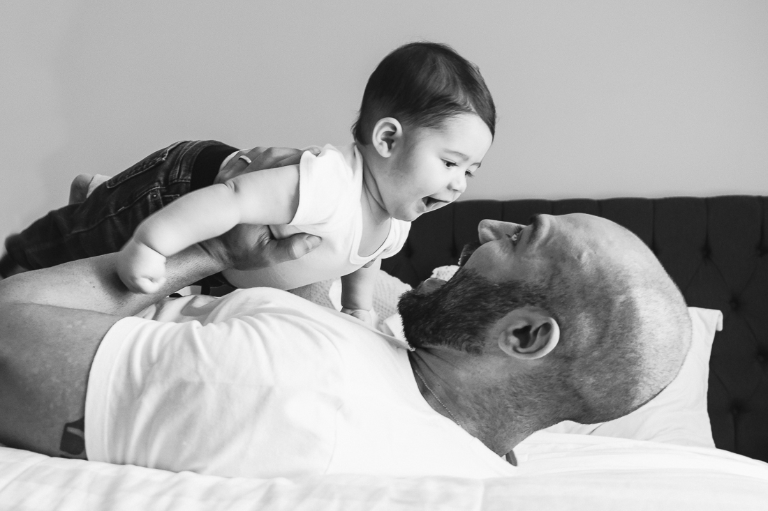 Foto de pai olhando e segurando o filho dentro do quarto deitado na cama no ensaio lifestyle em Sp