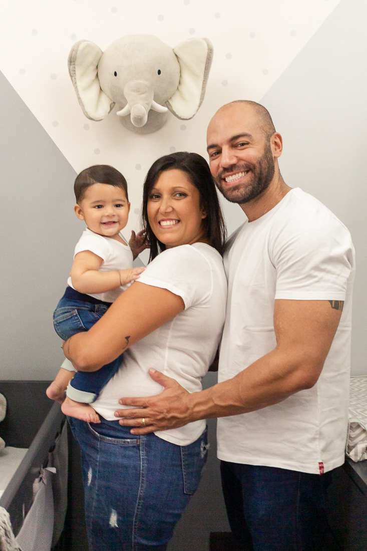 foto de pai e mãe no quarto com decoração de elefante segurando e sorrindo para o filho menino no ensaio de família na cidade de Sp