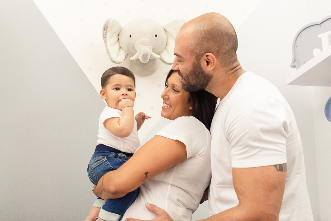 foto de pai e mãe no quarto com decoração de elefante segurando e sorrindo para o filho menino no ensaio de família na cidade de Sp