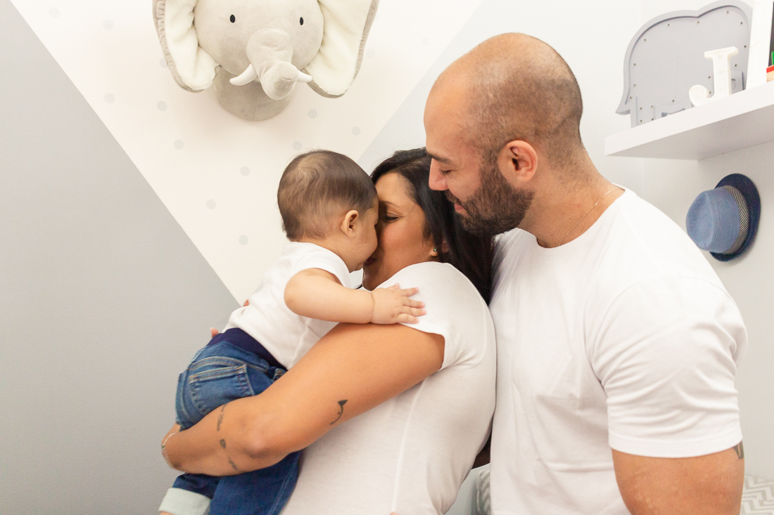 foto de pai e mãe no quarto com decoração de elefante segurando e beijando o filho menino no ensaio de família na cidade de Sp
