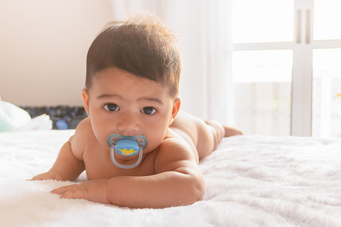 foto infantil de bebe deitado pelado na cama de chupeta no ensaio de família na cidade de Sp