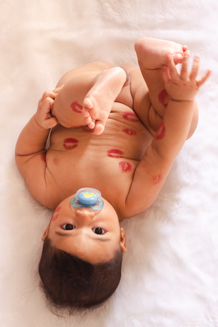 foto infantil de bebe deitado na cama do quarto dos pais pelado com beijo de batom no ensaio de família na cidade de Sp