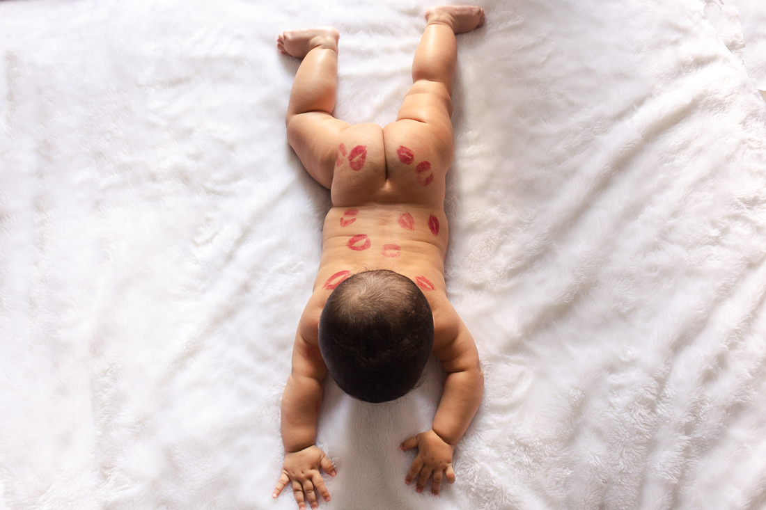 foto infantil de bebe deitado na cama do quarto dos pais com bumbum de fora  com beijo de batom no ensaio de família na cidade de Sp