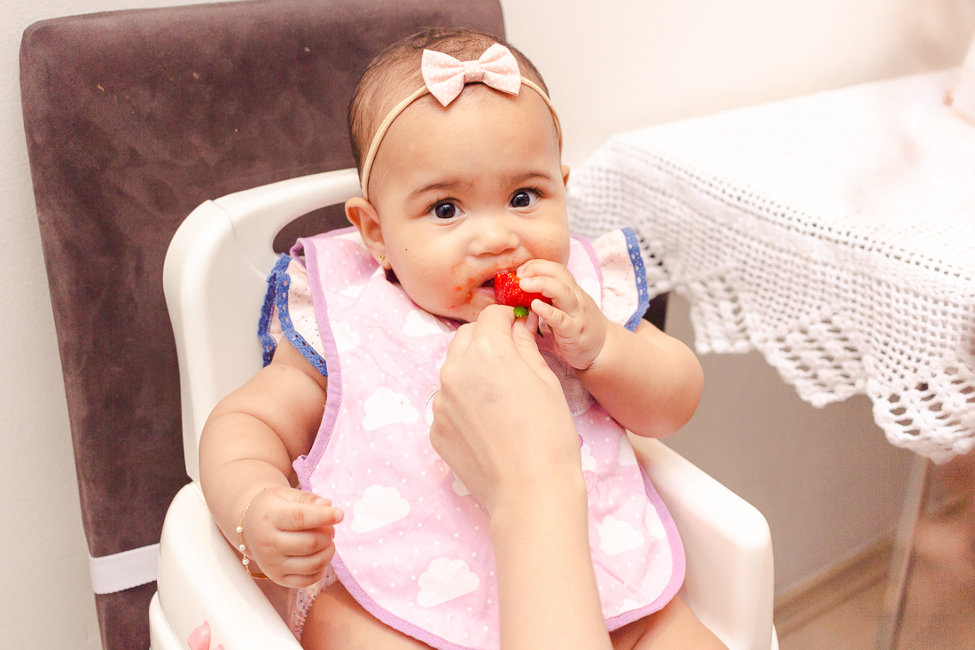 Foto bebe comendo fruta morango sentada na cadeirinha no ensaio lifestyle na cidade de São Paulo