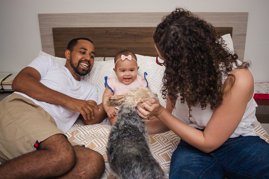 foto de pais com filha dentro do quarto deitados na cama no quarto com cachorro no ensaio de família