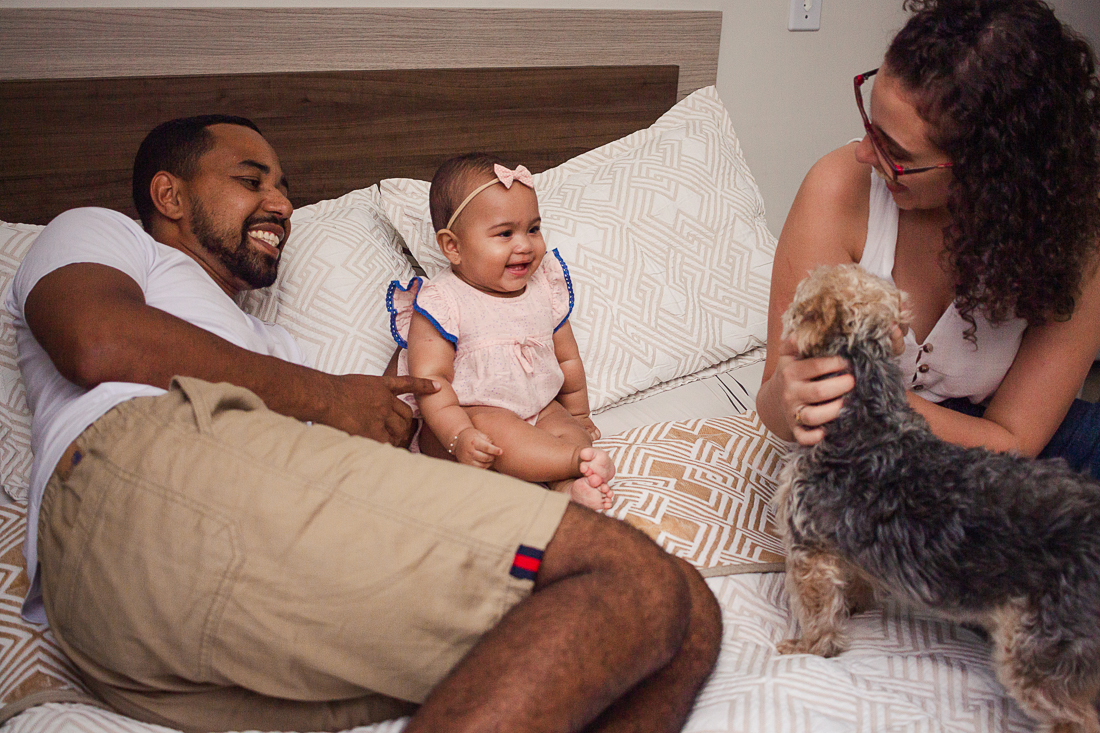 foto de pais com filha dentro do quarto deitados na cama no quarto com cachorro no ensaio de família