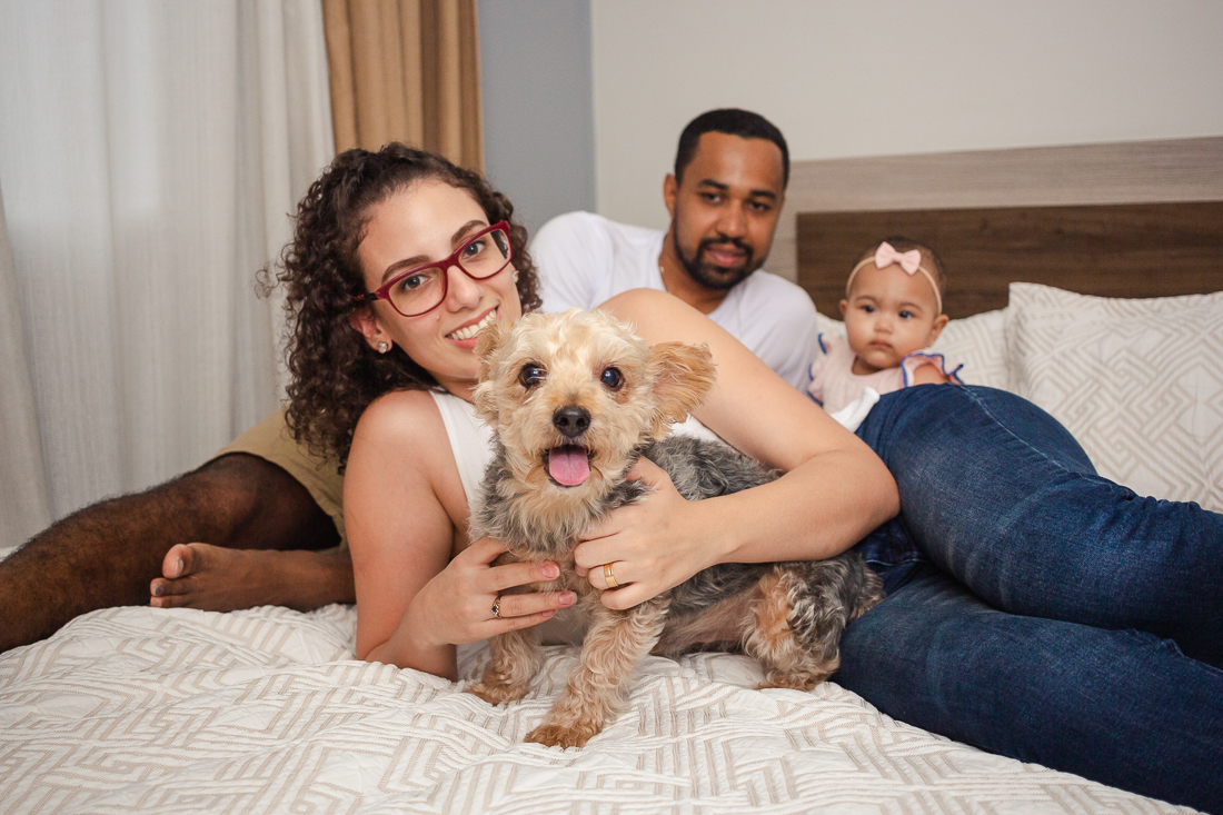 foto de pai, mãe e filha dentro do quarto deitados na cama no quarto com cachorro no ensaio de família