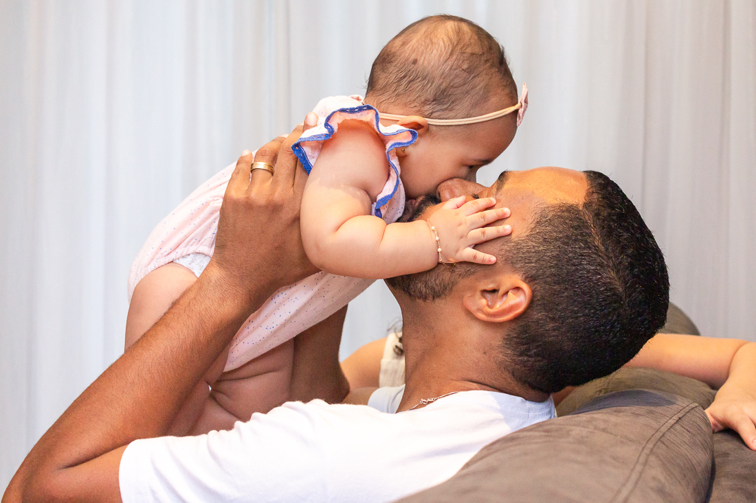 foto de pai beijando filha na sala de casa no ensaio lifestyle de família em Sp