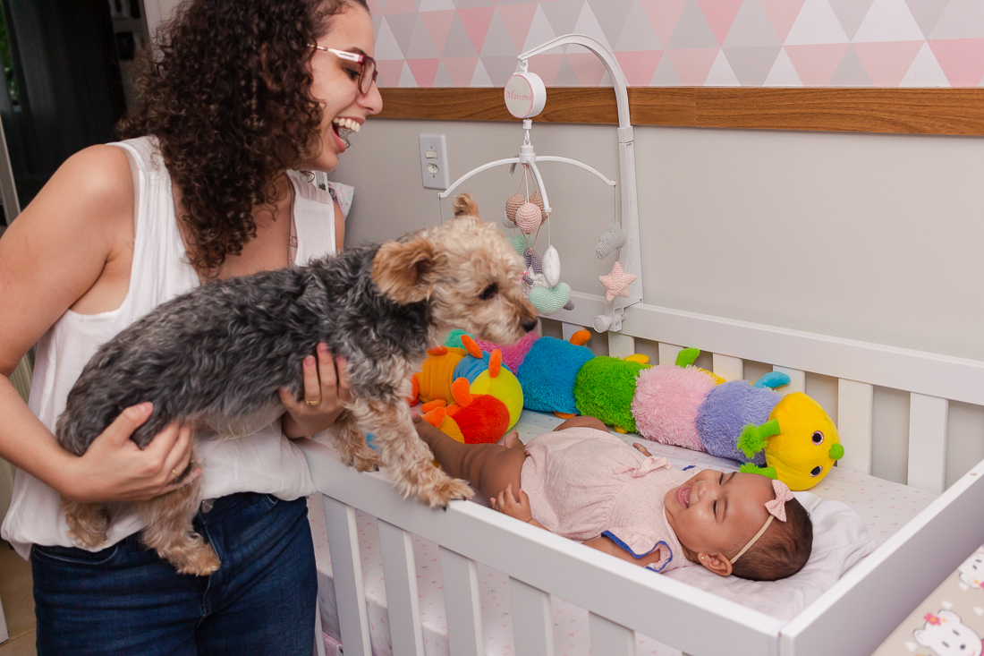 foto de mãe com cachorro no colo brincando com a bebe dentro do berço no quarto no ensaio de família na cidade de São Paulo