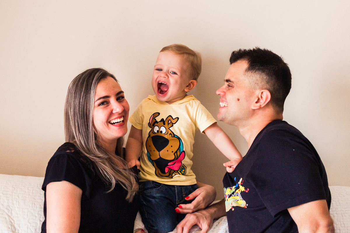 foto de criança sorrindo com os pais no sofá sala no ensaio de família em casa na cidade de Sp