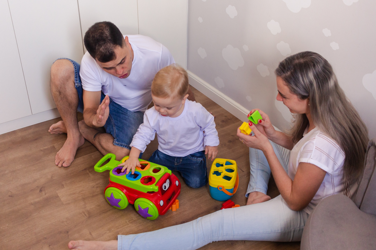 foto de filho brincando com os pais sentados no chão do quarto no ensaio de família em casa na zona leste de SP