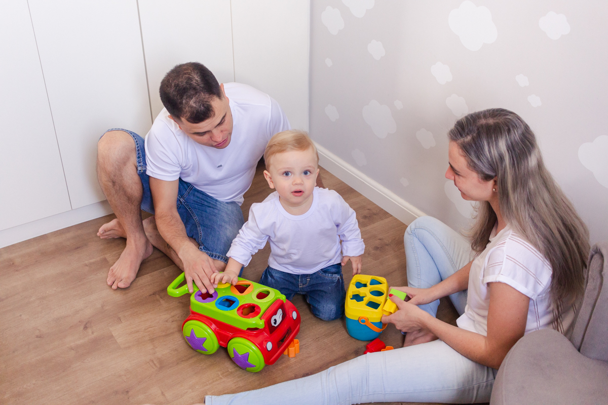 foto de filho brincando com os pais sentados no chão do quarto no ensaio de família em casa na zona leste de SP