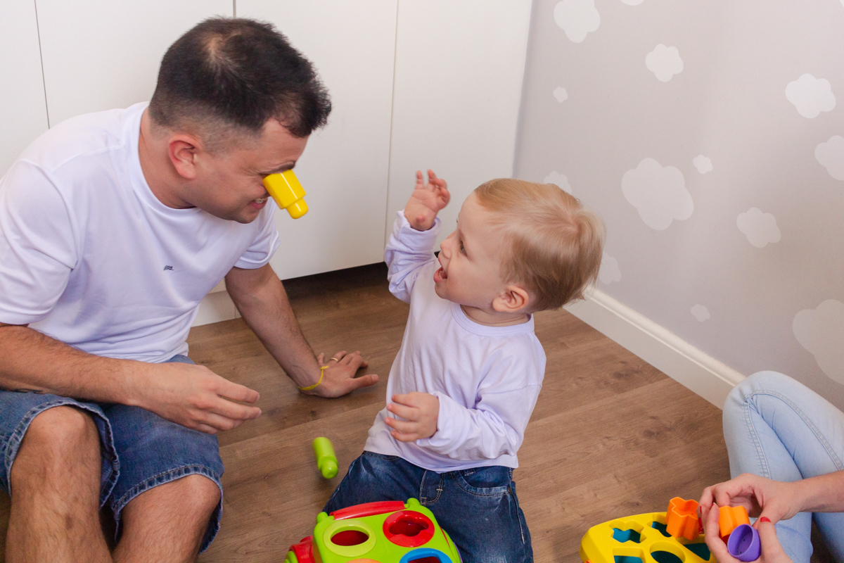 foto de filho brincando com o pai sentados no chão do quarto no ensaio de família em casa na zona leste de SP
