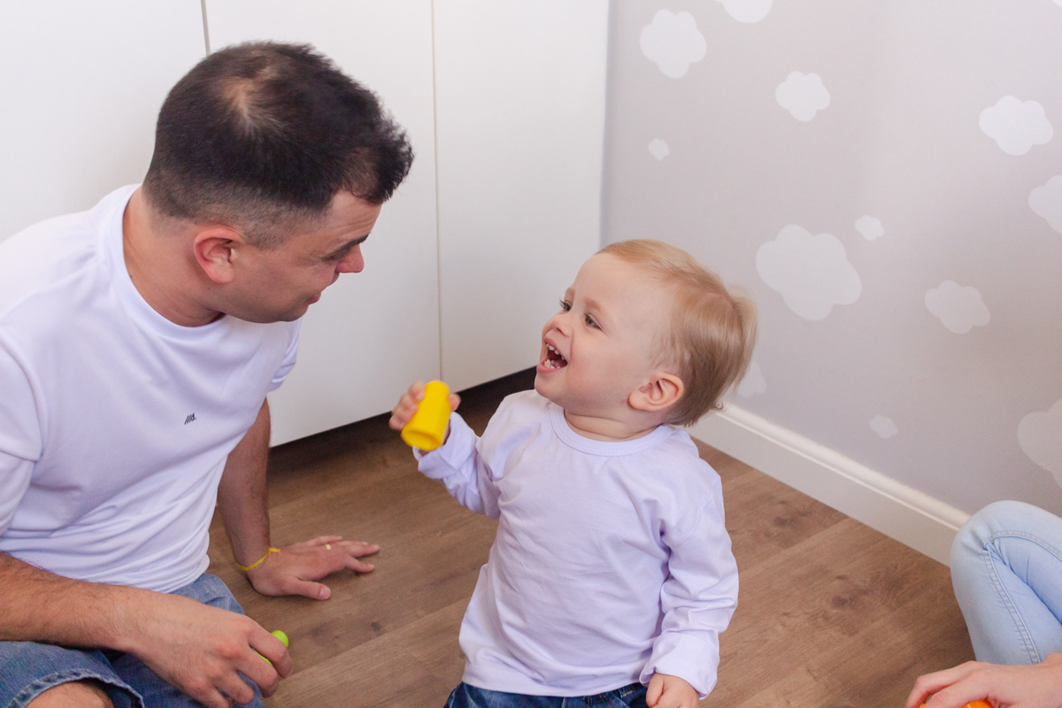 foto de filho brincando com o pai sentados no chão do quarto no ensaio de família em casa na zona leste de SP