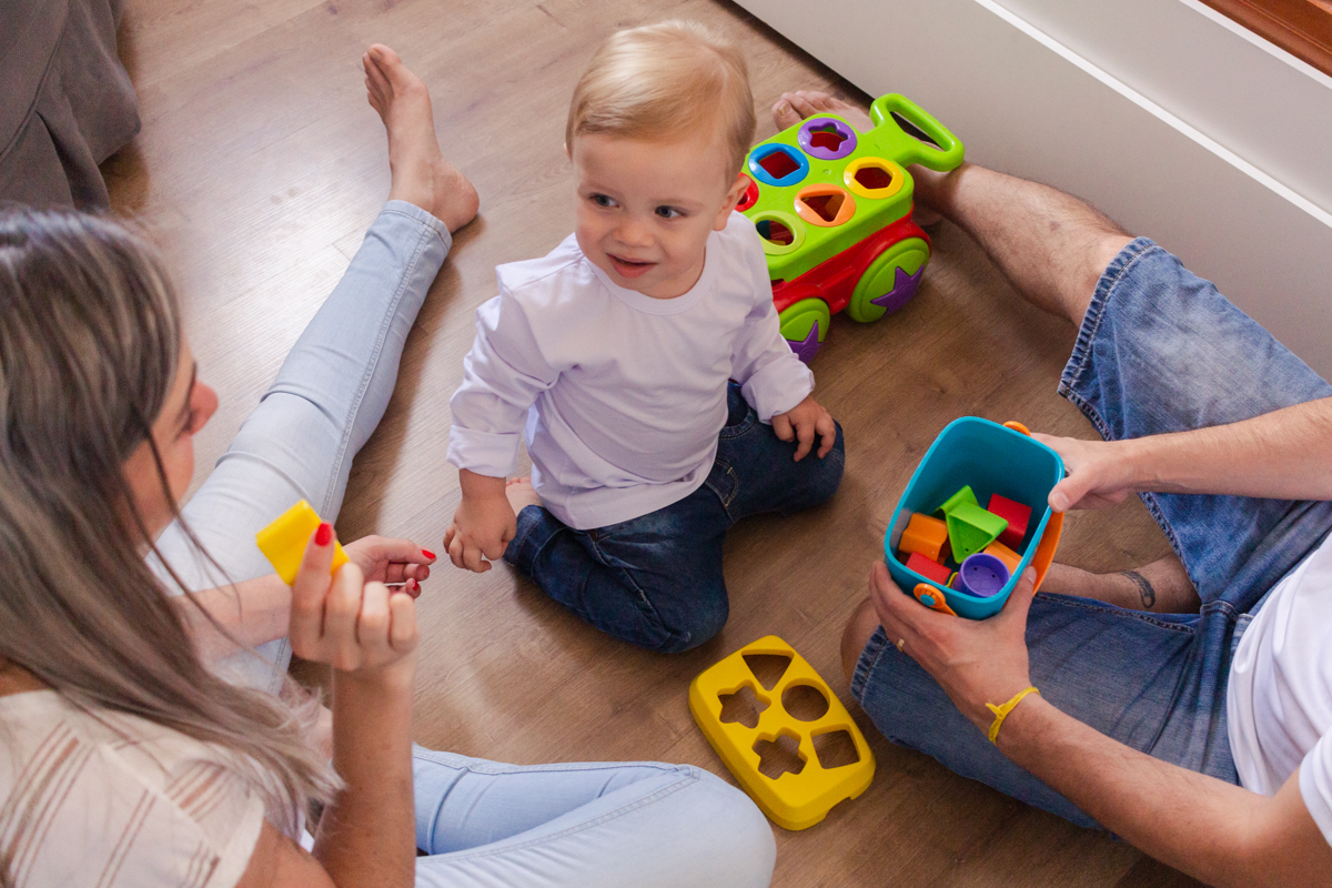 foto de filho brincando com os pais sentados no chão do quarto no ensaio de família em casa na zona leste de SP