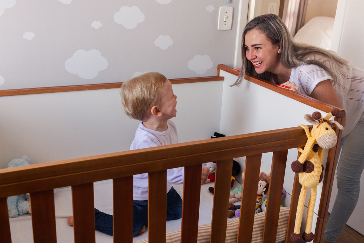 foto de criança dentro do do berço sorrindo para a mãe no ensaio de família em casa na cidade de Sp
